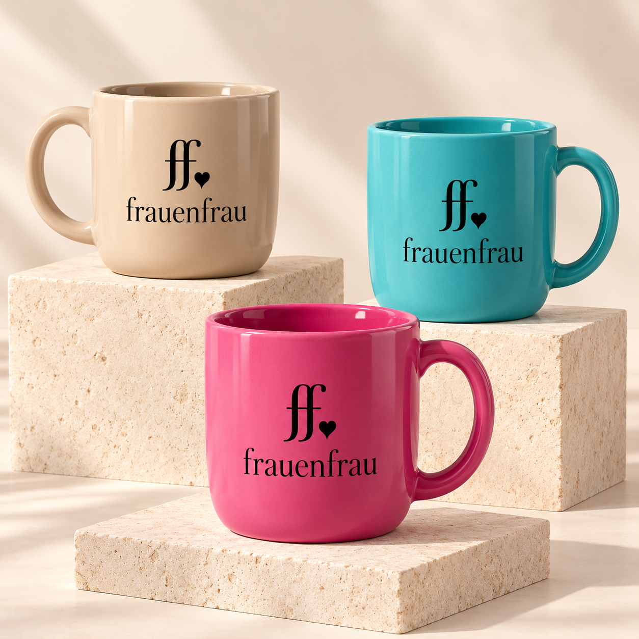 Drei hochwertige Kaffeebecher in Sand, Türkis und Fuchsia-Pink mit schwarzem ff-Herz-Logo und frauenfrau Schriftzug, auf hellen Steinsockeln präsentiert